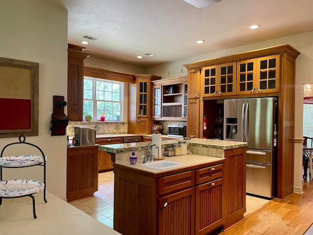 kitchen featuring appliances with stainless steel finishes, light wood-type flooring, backsplash, a kitchen island with sink, and sink