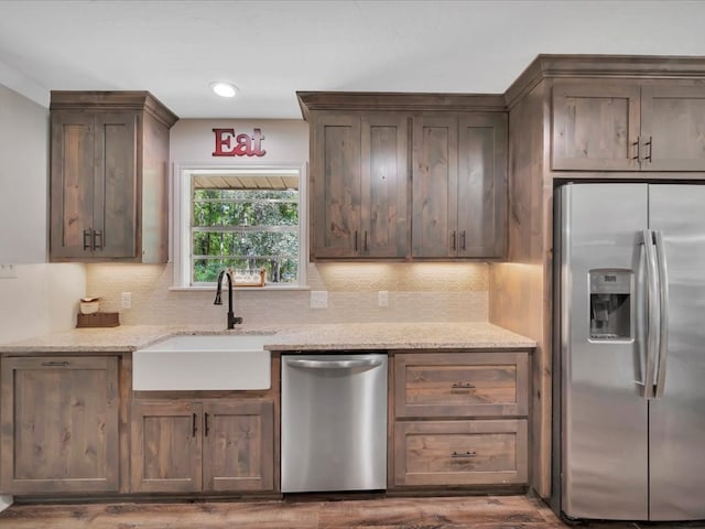 kitchen with light stone countertops, stainless steel appliances, a sink, dark brown cabinets, and decorative backsplash