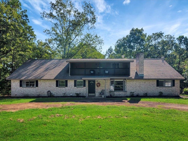 view of front of home with a chimney, brick siding, a balcony, and a front lawn