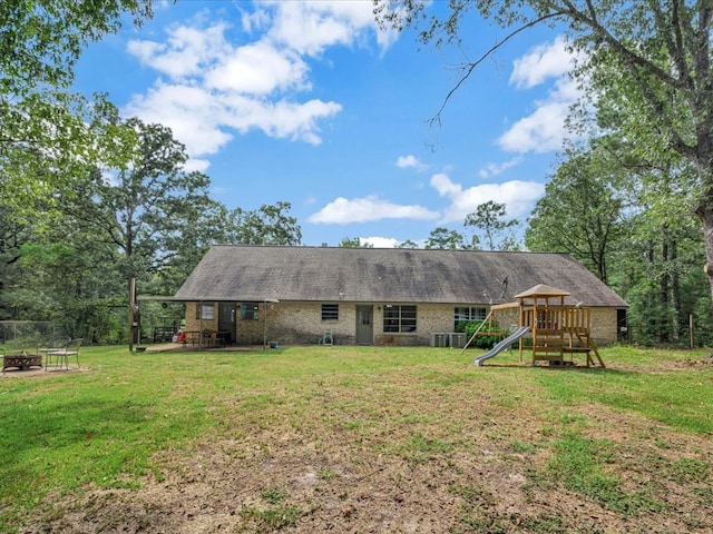 back of property featuring an outdoor fire pit, a patio area, a playground, and a lawn