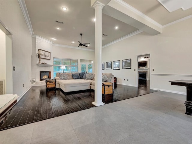 living room with ceiling fan, a large fireplace, decorative columns, hardwood / wood-style flooring, and ornamental molding