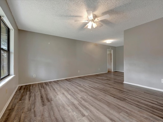 empty room featuring a textured ceiling, baseboards, a ceiling fan, and wood finished floors