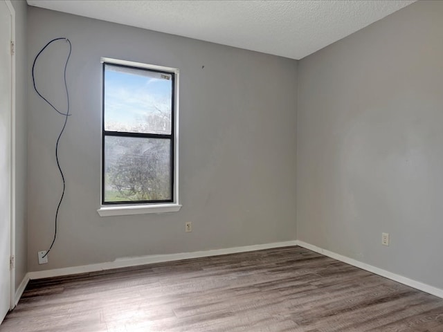 unfurnished room with a textured ceiling, baseboards, and wood finished floors