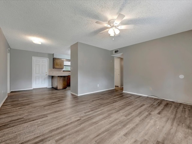 unfurnished living room featuring visible vents, a ceiling fan, a textured ceiling, wood finished floors, and baseboards