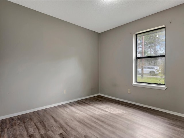 spare room with a textured ceiling, baseboards, and wood finished floors