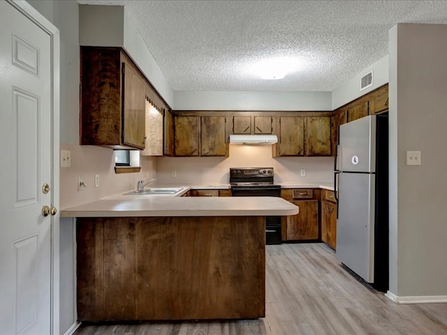 kitchen with black electric range oven, under cabinet range hood, a sink, freestanding refrigerator, and light countertops