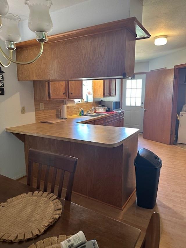 kitchen featuring tasteful backsplash, kitchen peninsula, sink, and light hardwood / wood-style flooring