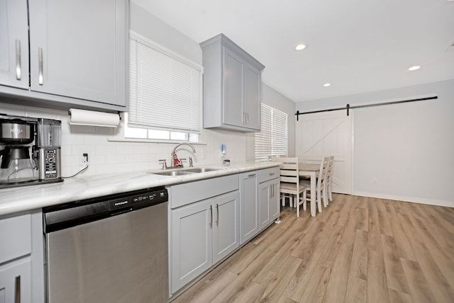 kitchen featuring dishwasher, sink, a barn door, light stone counters, and light wood-type flooring