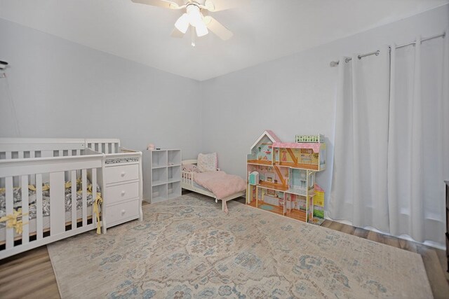 bedroom with hardwood / wood-style flooring, ceiling fan, and a crib