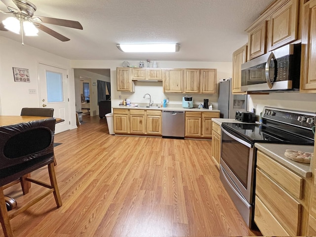 kitchen featuring appliances with stainless steel finishes, a textured ceiling, sink, light brown cabinets, and light hardwood / wood-style flooring