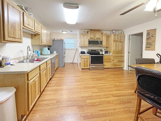 kitchen with sink, a textured ceiling, light brown cabinetry, appliances with stainless steel finishes, and light hardwood / wood-style floors