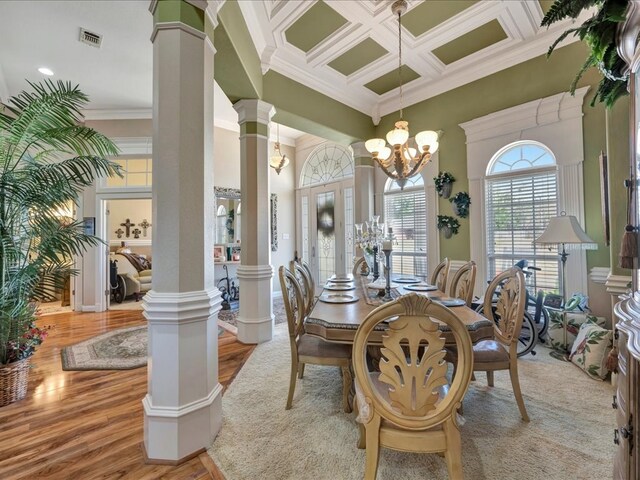 dining area featuring light wood-style flooring, coffered ceiling, an inviting chandelier, decorative columns, and crown molding