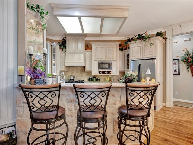 kitchen with stainless steel fridge, built in microwave, crown molding, premium range hood, and backsplash