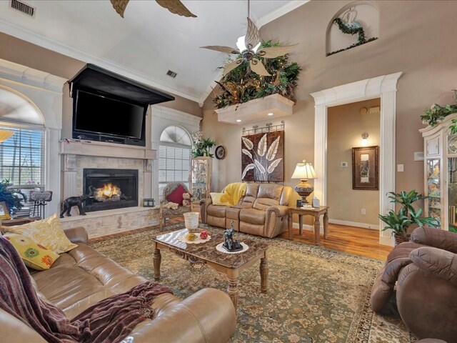 living room with a warm lit fireplace, visible vents, a ceiling fan, wood finished floors, and crown molding
