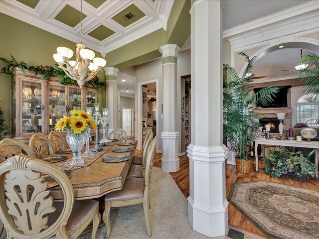 dining space featuring ornate columns, a warm lit fireplace, coffered ceiling, and crown molding