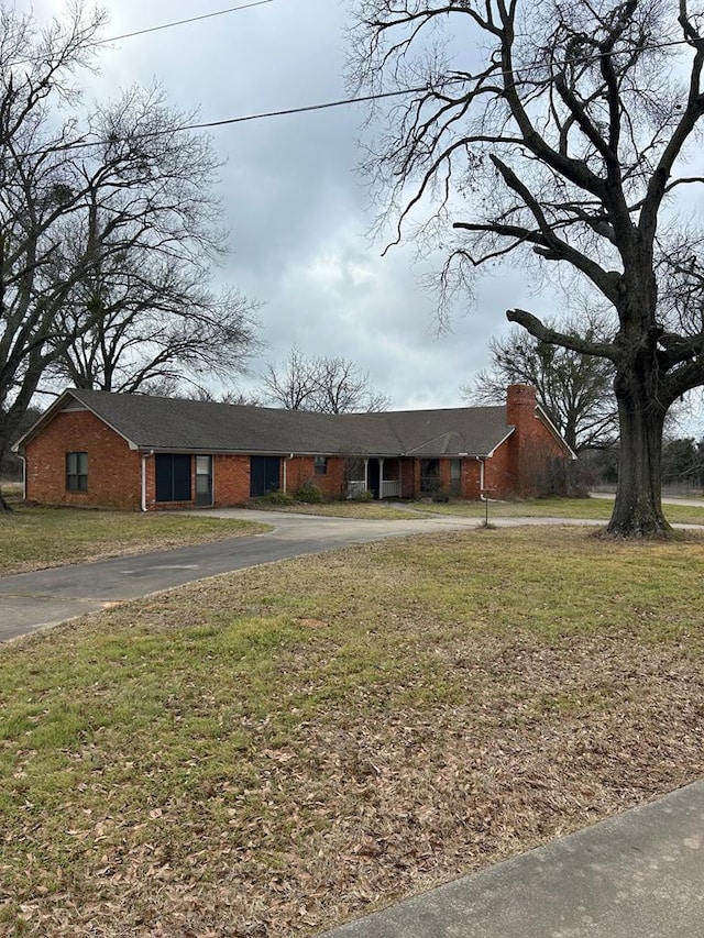 view of front of house featuring brick siding, driveway, a chimney, and a front lawn