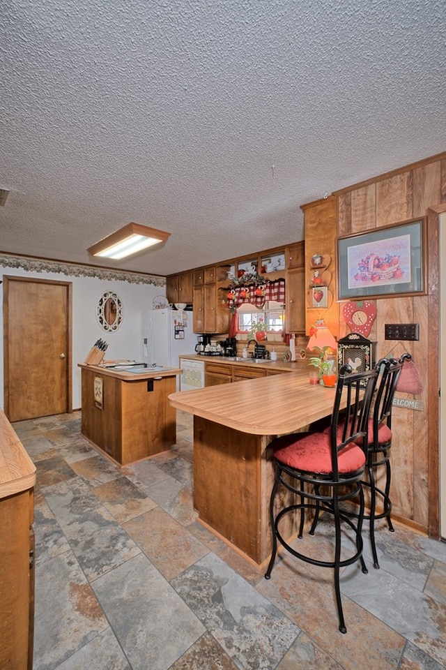 2105 Carters Ferry Rd, E Road, Milam, TX 75959 - kitchen with white fridge with ice dispenser, brown cabinetry, a peninsula, a textured ceiling, and stone tile flooring