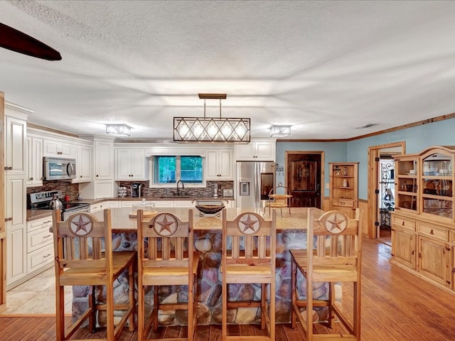 dining area featuring a textured ceiling, light hardwood / wood-style floors, sink, and crown molding