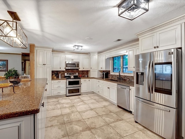 kitchen with sink, stainless steel appliances, dark stone countertops, pendant lighting, and white cabinets