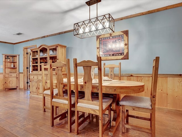 dining room with wood walls, wood-type flooring, and ornamental molding