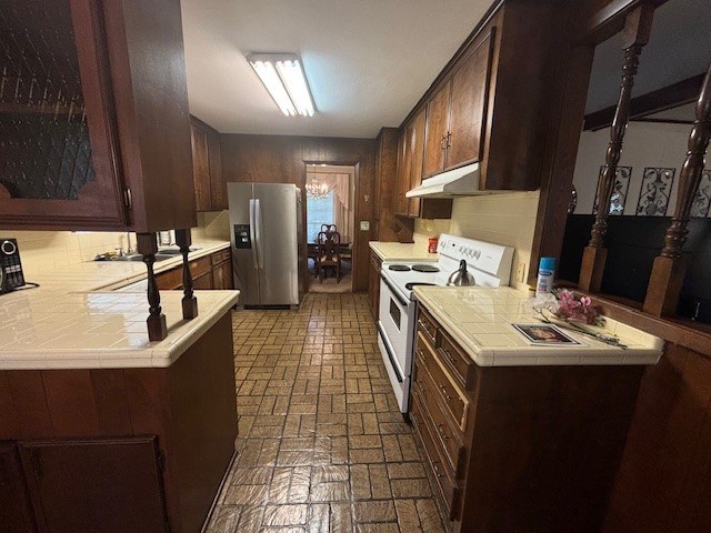 kitchen with kitchen peninsula, stainless steel refrigerator with ice dispenser, electric range, and tile counters