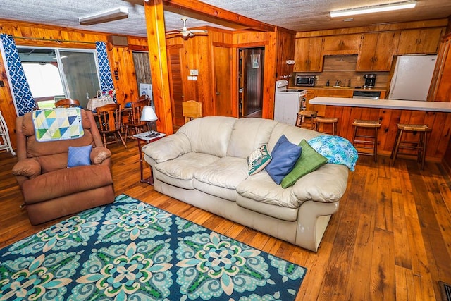 living area featuring wood-type flooring, ceiling fan, and wooden walls