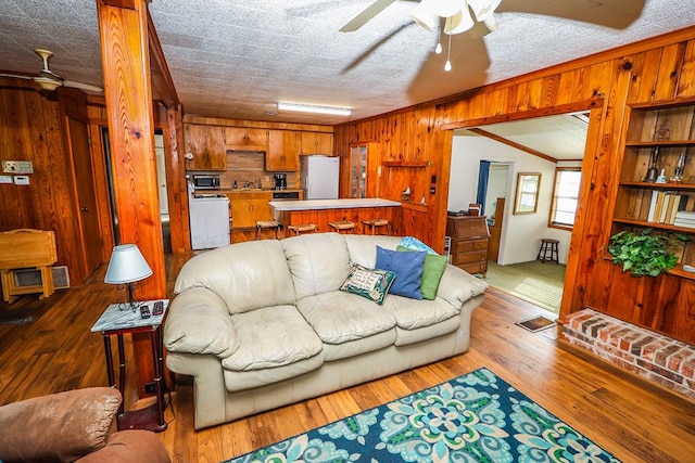 living area with visible vents, wood walls, ornamental molding, hardwood / wood-style flooring, and a ceiling fan