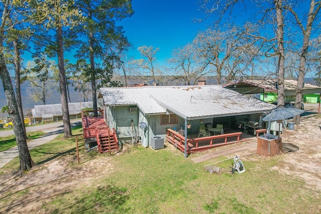 rear view of property with cooling unit, a yard, a deck, and metal roof