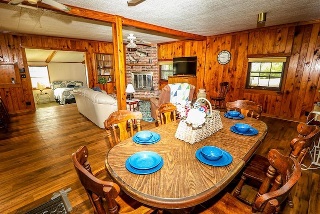 dining space featuring plenty of natural light, wood-type flooring, a brick fireplace, and wooden walls