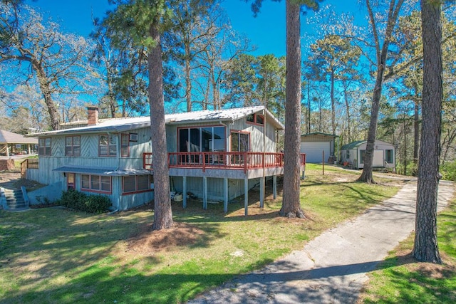 rear view of property featuring a garage, a wooden deck, a yard, a chimney, and an outbuilding