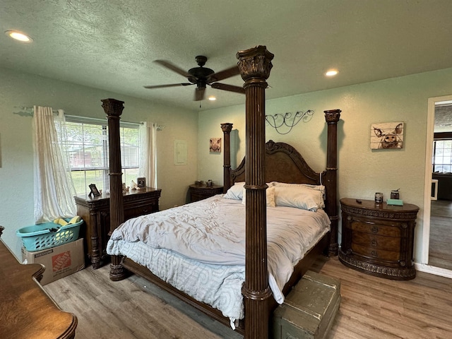 bedroom with a textured ceiling, light wood-type flooring, multiple windows, and ceiling fan