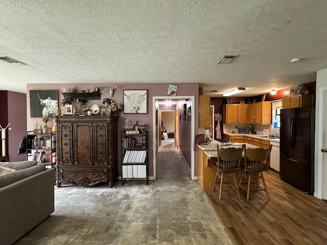 interior space with hardwood / wood-style floors, white dishwasher, black refrigerator, a textured ceiling, and a kitchen bar