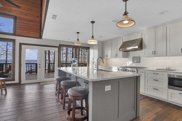 130 Boxwood Ln, Brookeland, TX 75931 - kitchen with wall chimney exhaust hood, stainless steel microwave, dark wood-style flooring, a breakfast bar, and tasteful backsplash