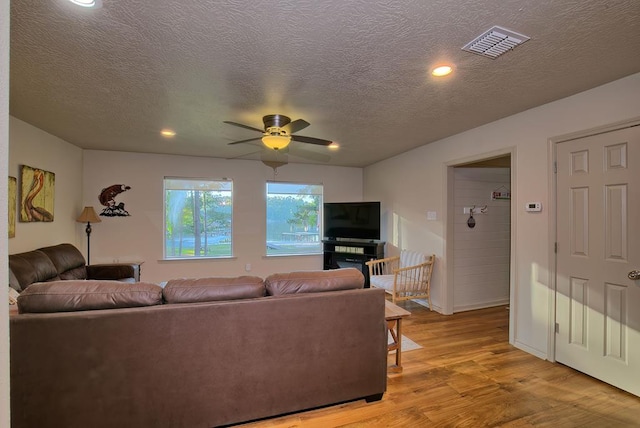 living room featuring ceiling fan, light hardwood / wood-style floors, and a textured ceiling