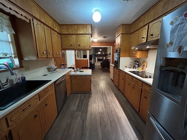kitchen featuring a sink, brown cabinets, under cabinet range hood, and appliances with stainless steel finishes