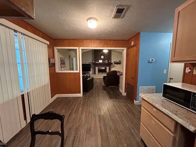 corridor featuring baseboards, wooden walls, visible vents, and dark wood-type flooring