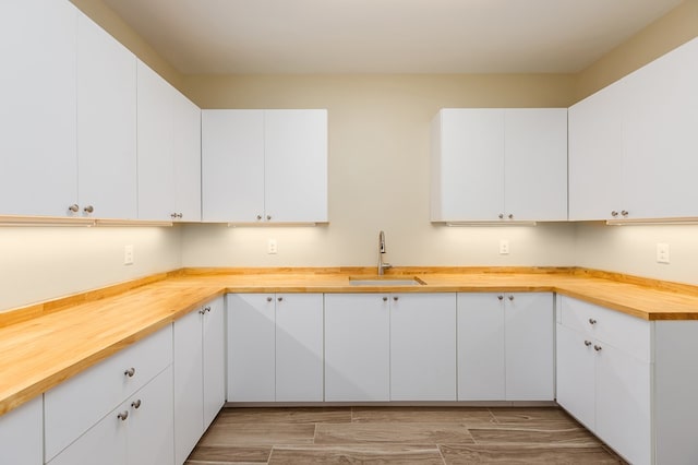 kitchen featuring butcher block counters, white cabinetry, and sink