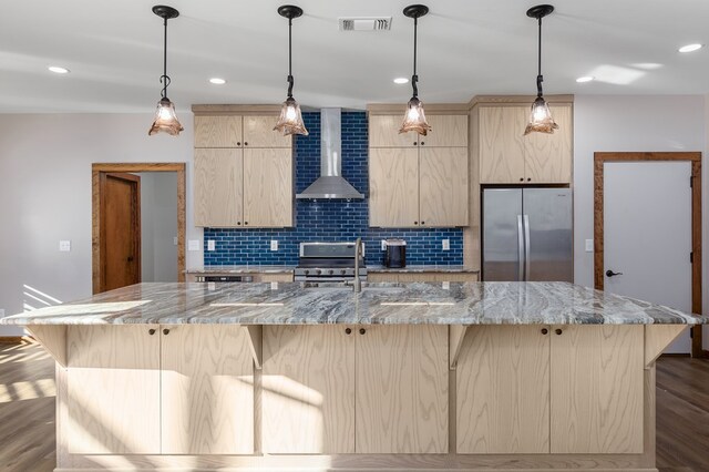 kitchen featuring light stone countertops, light brown cabinets, stainless steel appliances, and wall chimney range hood