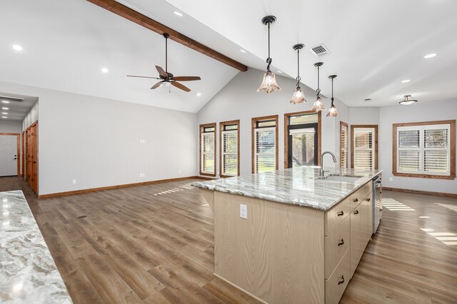 kitchen with sink, light stone counters, light hardwood / wood-style flooring, decorative light fixtures, and a kitchen island with sink