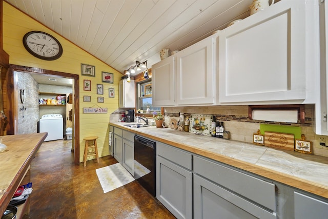 kitchen featuring dishwasher, white cabinets, wooden walls, vaulted ceiling, and washer / dryer