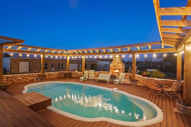 pool at night featuring an outdoor stone fireplace and a deck