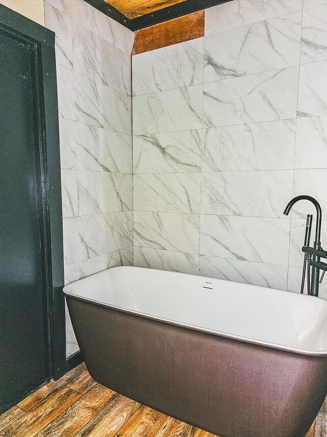 bathroom featuring wood-type flooring, a bathtub, and tile walls