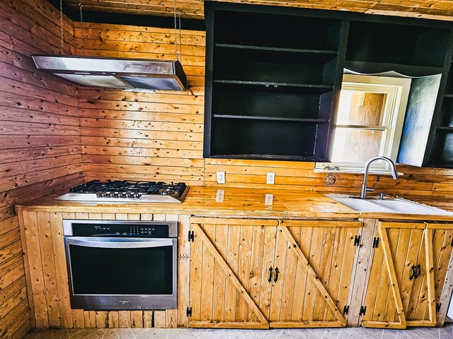 kitchen featuring ventilation hood, sink, wooden walls, butcher block counters, and stainless steel appliances