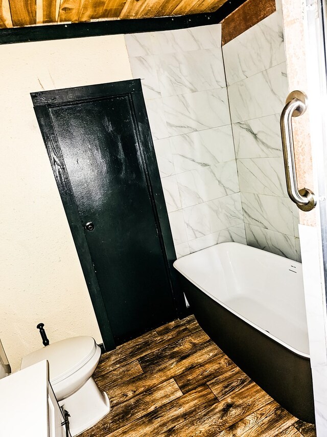 bathroom with toilet, wood-type flooring, and a bath