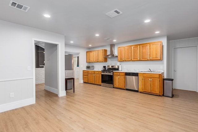 kitchen with light wood-type flooring, wall chimney range hood, sink, and appliances with stainless steel finishes