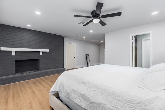 bedroom featuring a fireplace, ceiling fan, and light hardwood / wood-style flooring