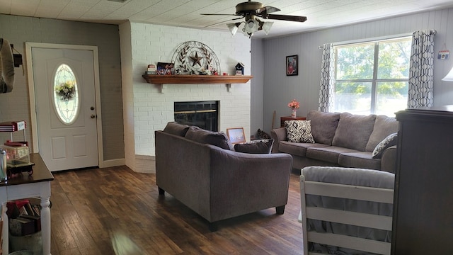 living room with ceiling fan, dark wood-type flooring, brick wall, and a brick fireplace