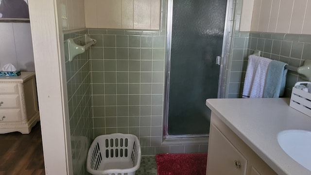 bathroom with wood-type flooring, vanity, a shower with door, and tile walls