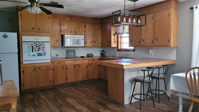 kitchen with white appliances, dark wood-type flooring, sink, decorative backsplash, and kitchen peninsula