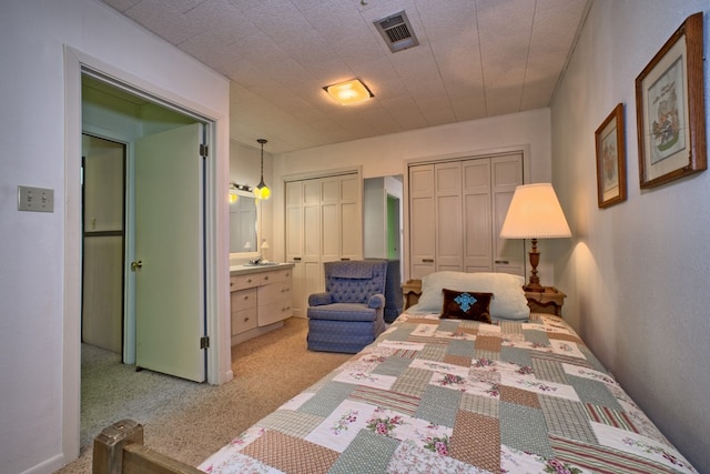 bedroom with two closets, visible vents, and light colored carpet